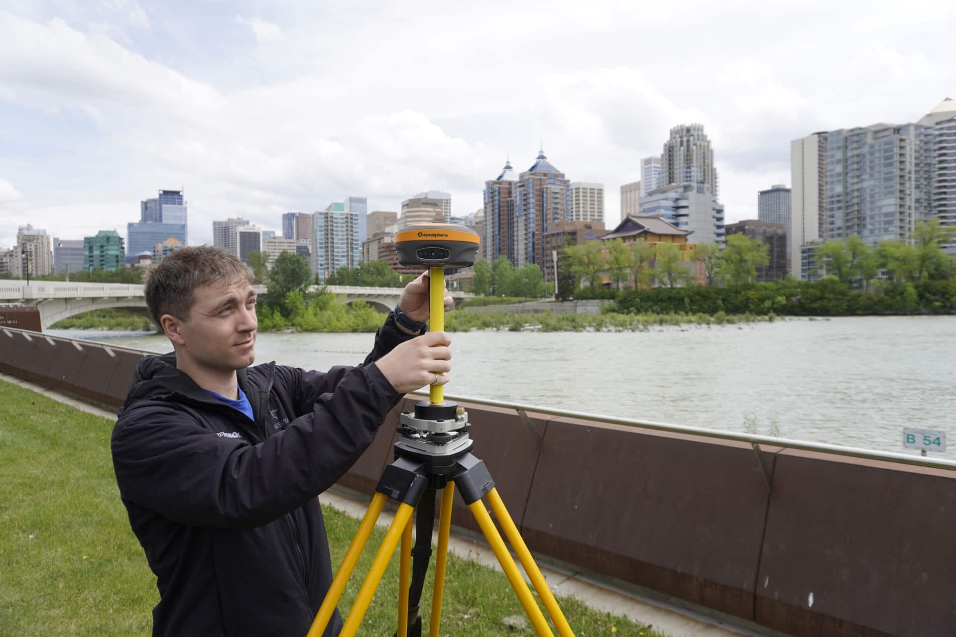 A man sets up a Hemisphere S631 GNSS Receiver in front of a city.