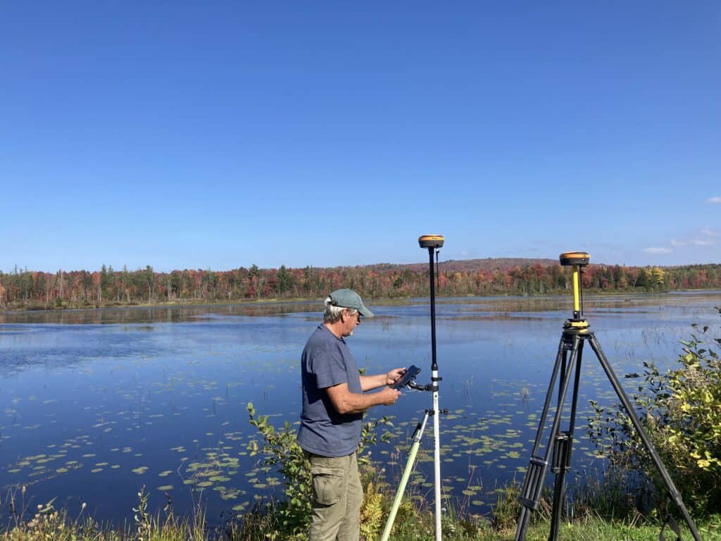 Surveyor using GNSS receivers on aluminum and fiberglass surveying rods near lakeside control point