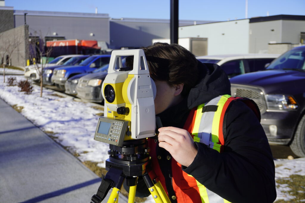 Surveyor using a total station on a tripod for precise line-of-sight measurement in a construction area