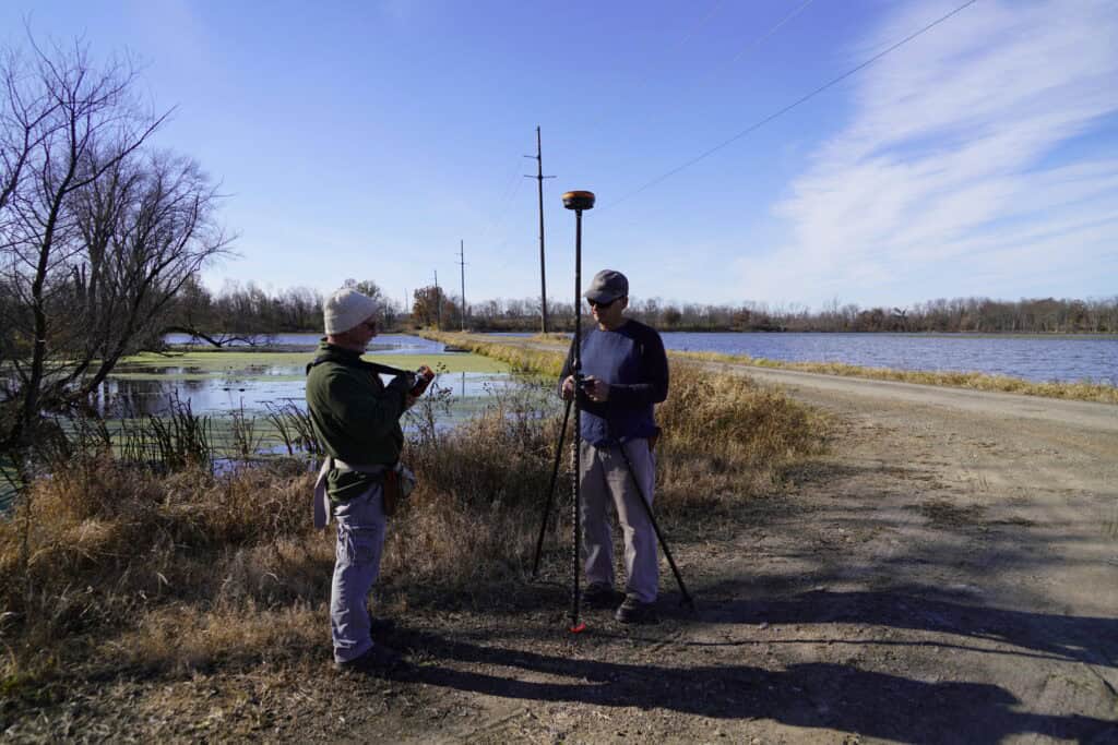 Surveyors using Hemisphere GNSS receiver for RTK land surveying near waterway