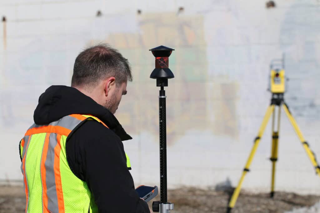 Surveyor using GNSS rover and total station for construction site layout and staking